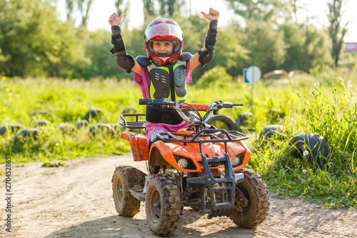 The little girl rides a quad bike. A mini quad bike is a cool girl in a helmet and protective clothing. Electric quad bike electric car for children popularizes green technology photo