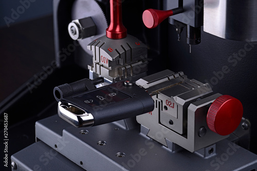 Close view of key copying machine with key. Duplicate machine make new key. Locksmith theme. Blank keys for cutting. Black modern car door opener.