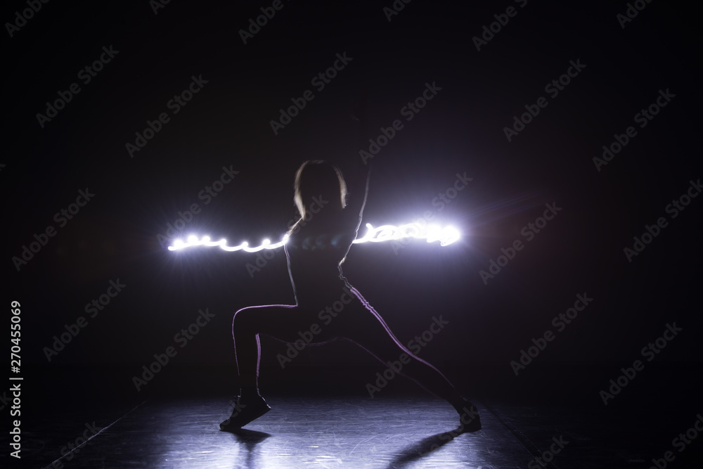 Modern art dancer, dancing in front of a black background with neon blue light while steching and twisting her body.
