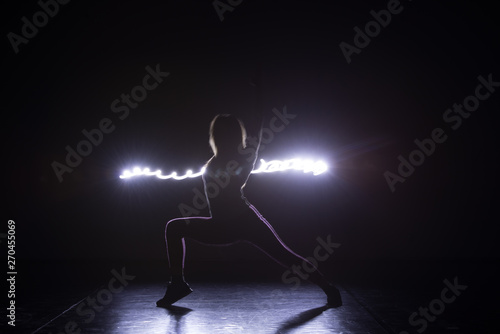 Modern art dancer, dancing in front of a black background with neon blue light while steching and twisting her body.