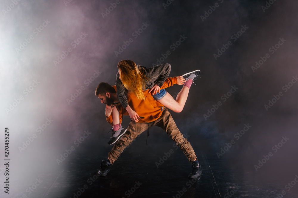 Strong male dancer and an elegant female dancer perform an exotic and unique dance moves in front of a black background while wearing urban clothes.