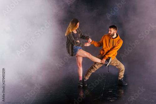 Couple dancing modern dance and showing off their leg stretch moves.Black background while the couple is dressed in urban colorful clothes..