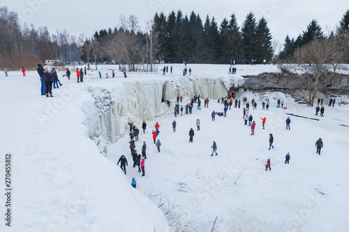 Jagala, Estonia - February 15, 2018: People are walking in the ice cave of frozen waterfall on a sunny day. A frozen Jagala Waterfall. Winter entertainment.