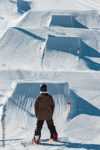 Snowboarders waiting for their turn in front of the kickers in the snowpark