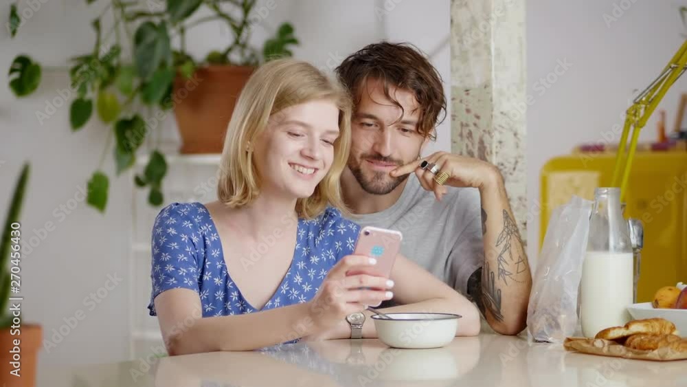Couple of different ethnicity enjoying online internet content at breakfast time together, staring at smartphone display always connected to friends during early morning blonde girl holding gadget Couple of different ethnicity enjoying online internet content at breakfast time together, staring at smartphone display always connected to friends during early morning blonde girl holding gadget