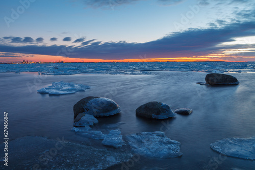Sunset over frozen coast of the Baltic sea. Calm winter moment. Icy boulders on the blue background.