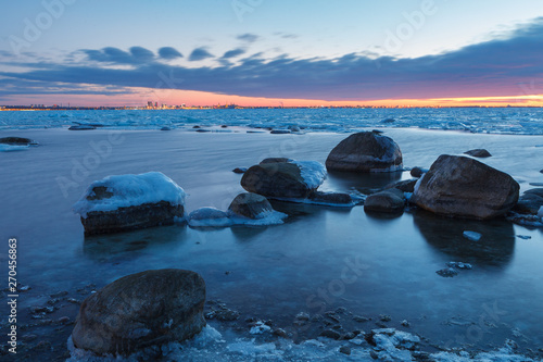 Sunset over frozen coast of the Baltic sea. Calm winter moment. Icy boulders on the blue background.