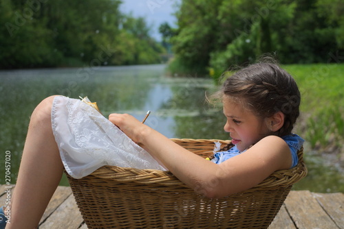 attractive pretty girl lying down and writing in basket while enjoying on riverbank