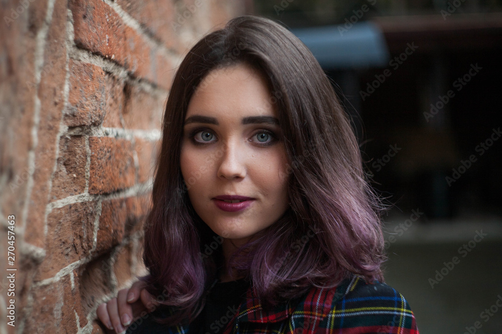 Fototapeta premium beautiful brunette in a plaid jacket at the brick wall