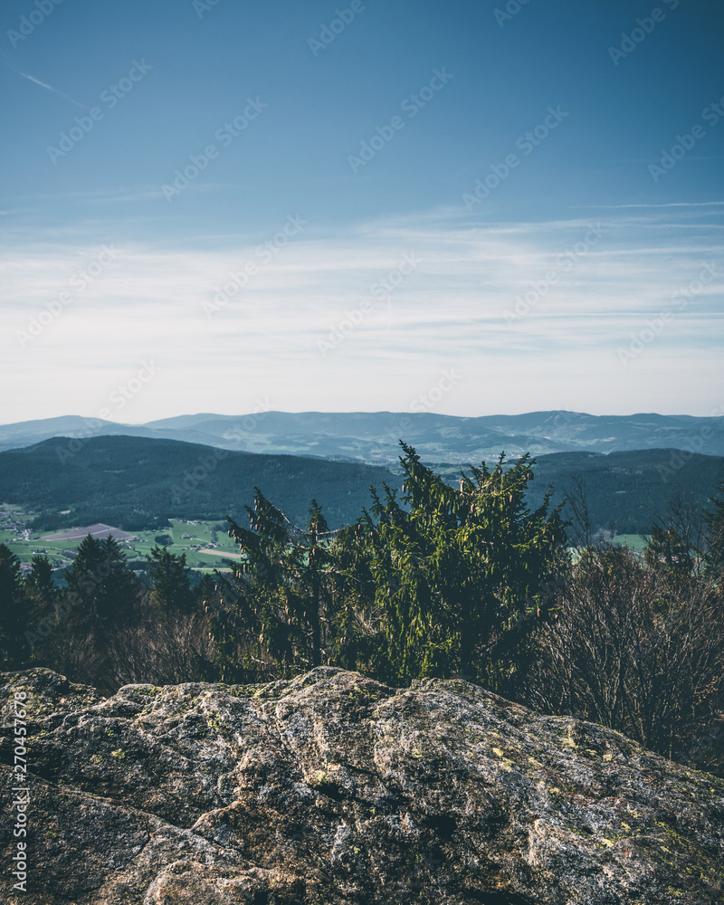View from the top of a mountain into the valley with clouds in the blue sky and beautiful green trees and lots of rocks