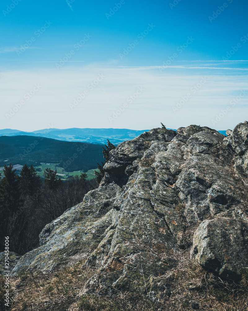 View from the top of a mountain into the valley with clouds in the blue sky and beautiful green trees and lots of rocks