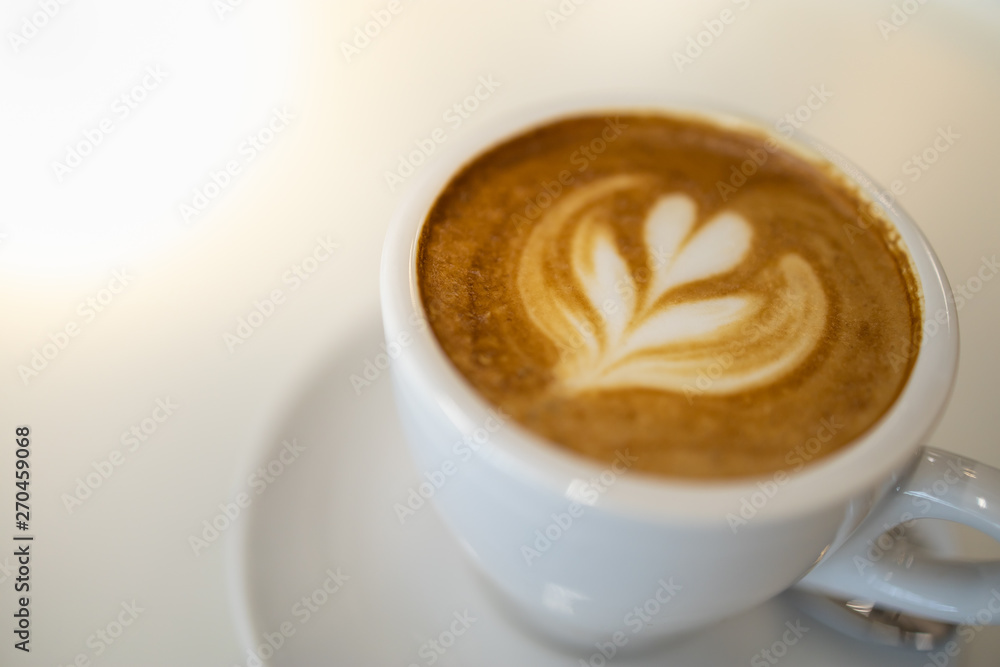 Close up of white cup of hot coffee latte with milk foam heart and flower shape art on white table. Close up of white cup of hot coffee latte with milk foam heart and flower shape art on white table.