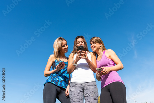 Three happy young women watching the smart phone with a blue sky