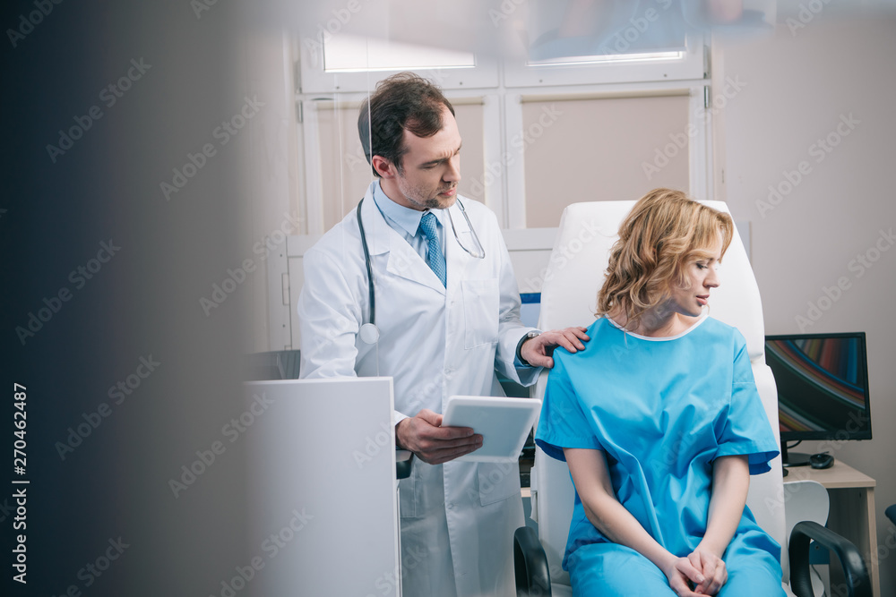 selective focus of doctor holding digital tablet and touching shoulder of upset woman selective focus of doctor holding digital tablet and touching shoulder of upset woman