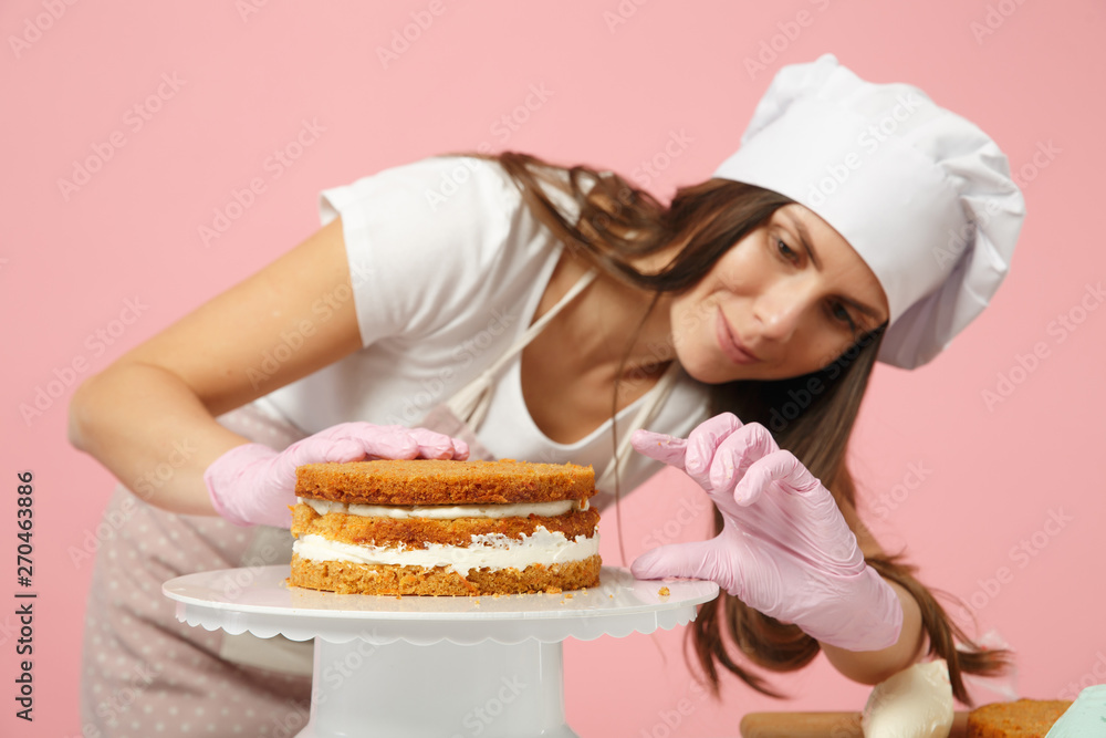 Chef cook confectioner or baker in white t-shirt, toque chefs hat cooking at table isolated on pink pastel background in studio. Cream application, cake making process. Mock up copy space food concept Chef cook confectioner or baker in white t-shirt, toque chefs hat cooking at table isolated on pink pastel background in studio. Cream application, cake making process. Mock up copy space food concept