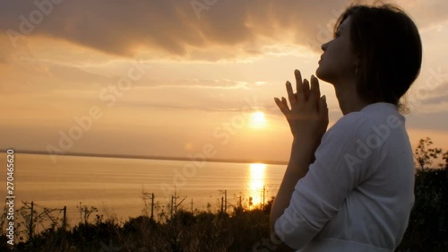 silhouette of young woman figure praying to God at sunset, the girl folded her hands at the chin in the field, concept of religion