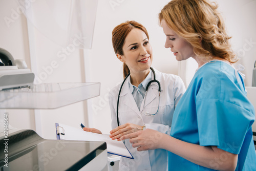 smiling radiologist holding clipboard while standing near patient reading diagnosis on clipboard