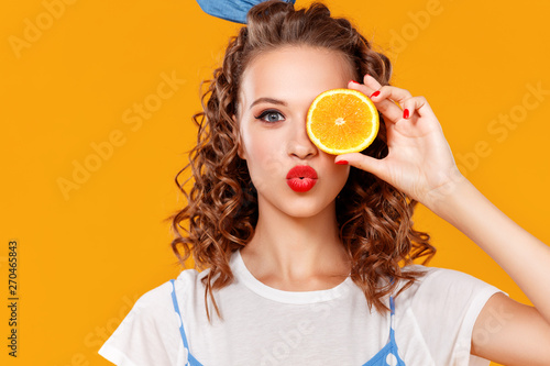 cheerful young curly woman girl with   orange   on  yellow   background.