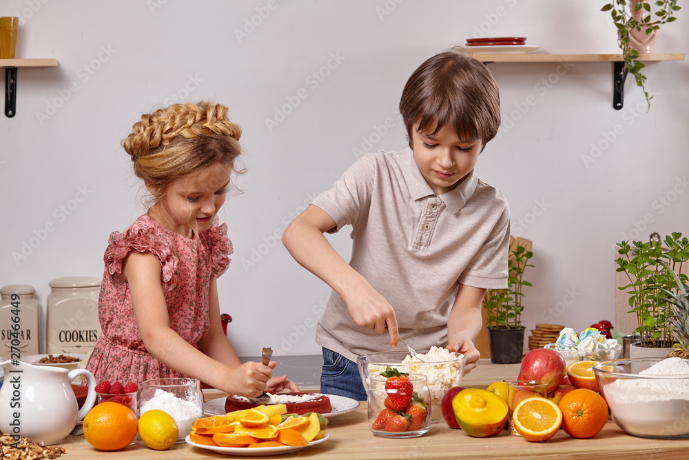 Little friends are making a cake together at a kitchen against a white wall with shelves on it. Little friends are making a cake together at a kitchen against a white wall with shelves on it.