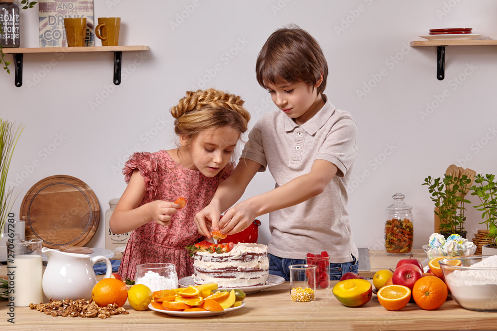 Little friends are making a cake together at a kitchen against a white wall with shelves on it.