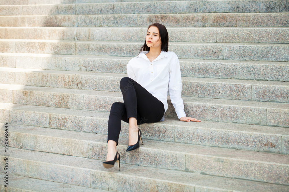 Young beautiful brunette woman in white shirt sitting on stone steps Young beautiful brunette woman in white shirt sitting on stone steps