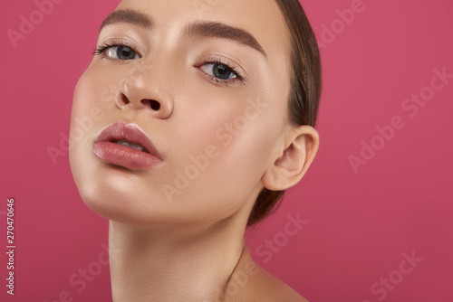 Attractive young woman with full lips posing against pink background