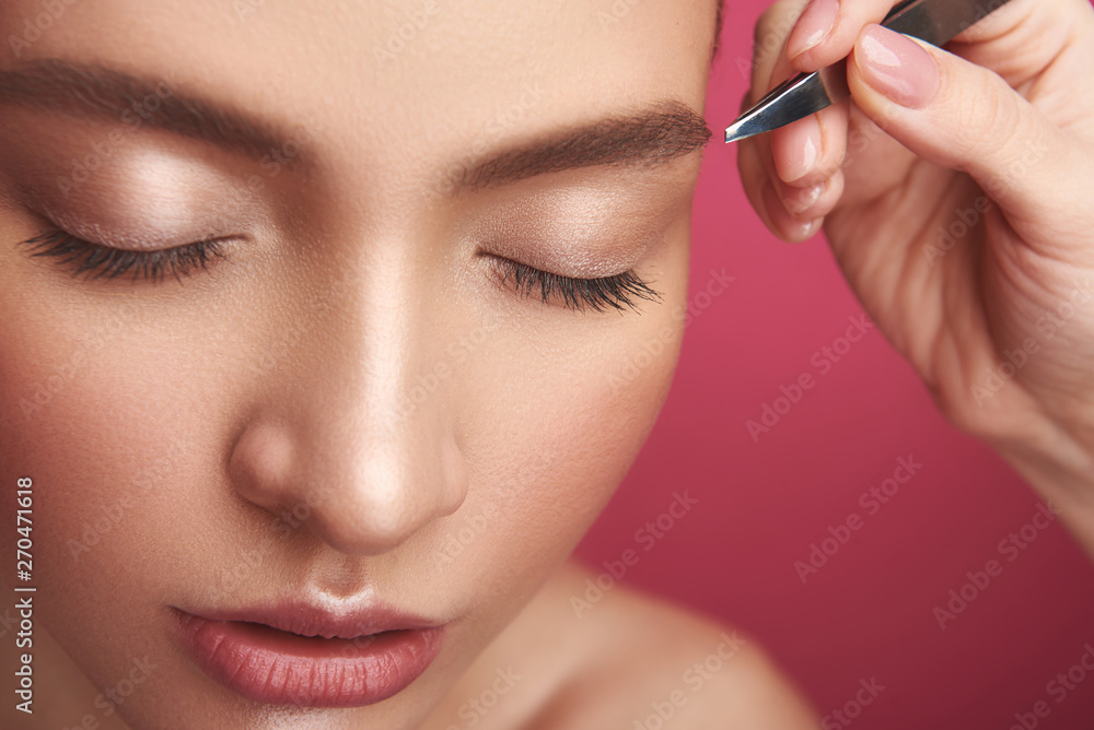 Beautician arm plucking lady eyebrows with tweezers