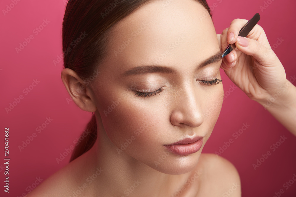Beautician plucking young lady eyebrows with tweezers