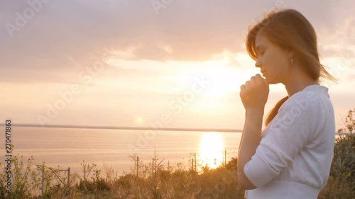 face profile of young beautiful woman turning to God in nature at sunset, the girl praying folded her hands at the chin, concept of religion