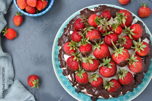 Chocolate cake with strawberries and cream located on a dark background, top view