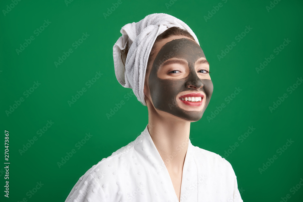 Cheerful girl with towel on her head using clay facial mask Cheerful girl with towel on her head using clay facial mask