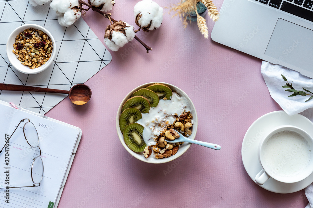 Healthy breakfast bowl milk laptop and organizer on pink table background  concept, morning meal at work in home office, natural nutrition food with  computer concept, freelancer workplace, top view Stock Photo