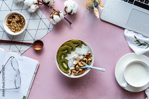 Healthy breakfast bowl milk laptop and organizer on pink table background concept, morning meal at work in home office, natural nutrition food with computer concept, freelancer workplace, top view