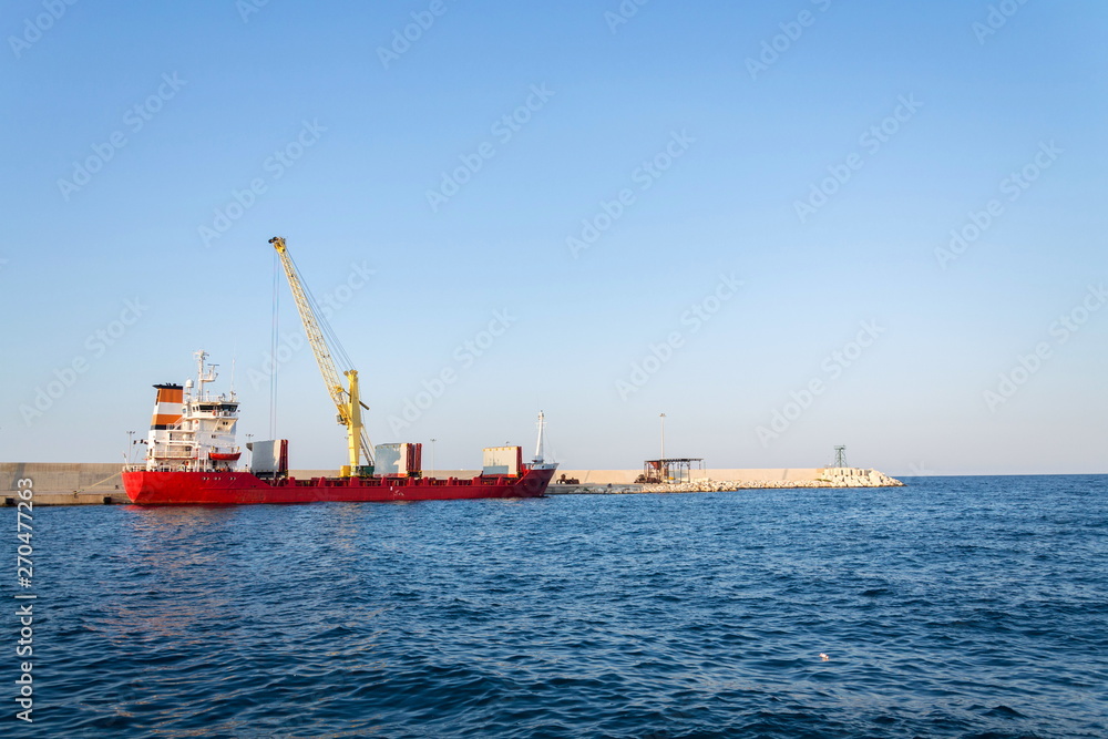 Yellow crane unloading sand from large freighter cargo ship in harbor, freight digitalization, transportation efficiency, sand shortage concept, sunny day copy space