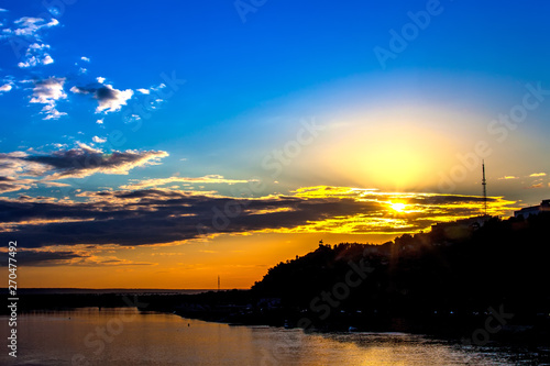 Silhouette of monument to Salawat Yulaev against a bright yellow blue sky with clouds and orange sun disk at city sunset on the river bank. Salavat Yulayev, Ufa, Bashkortostan, Russia. photo