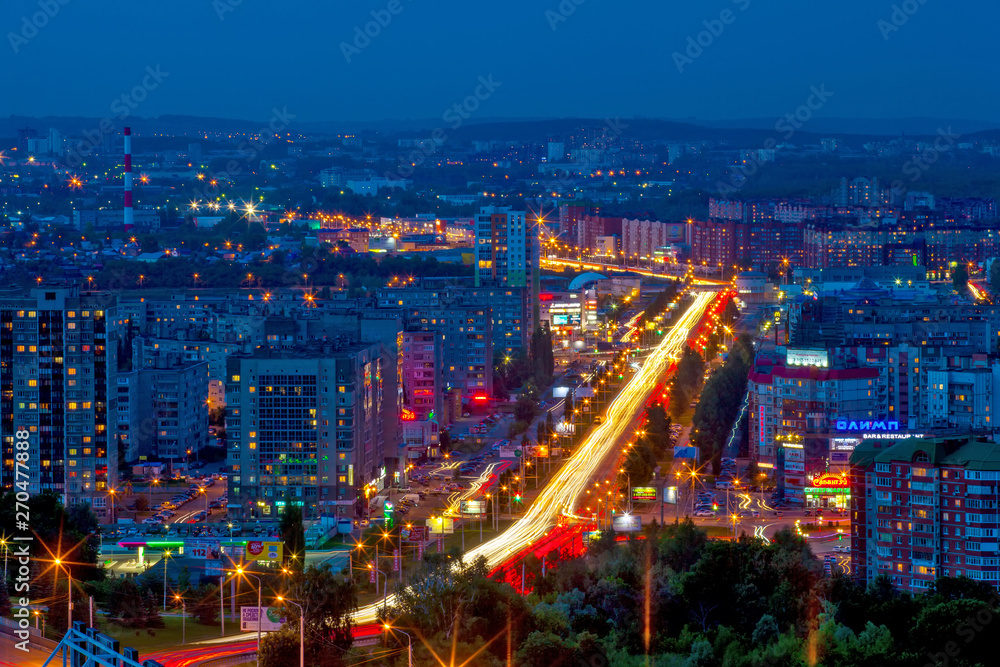 Panorama of the night modern city, the central street in the yellow light trails of passing cars between the sleeping areas in blue twilight color. Ufa, Bashkortostan, Russia - June 2015.