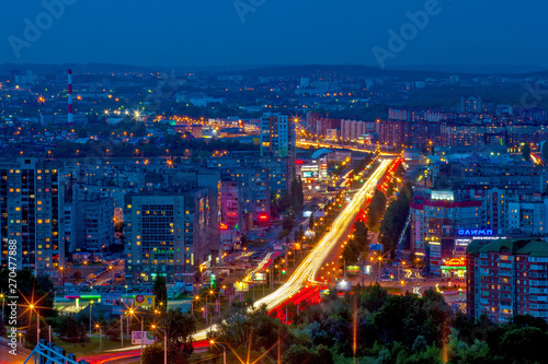 Panorama of the night modern city, the central street in the yellow light trails of passing cars between the sleeping areas in blue twilight color. Ufa, Bashkortostan, Russia - June 2015.