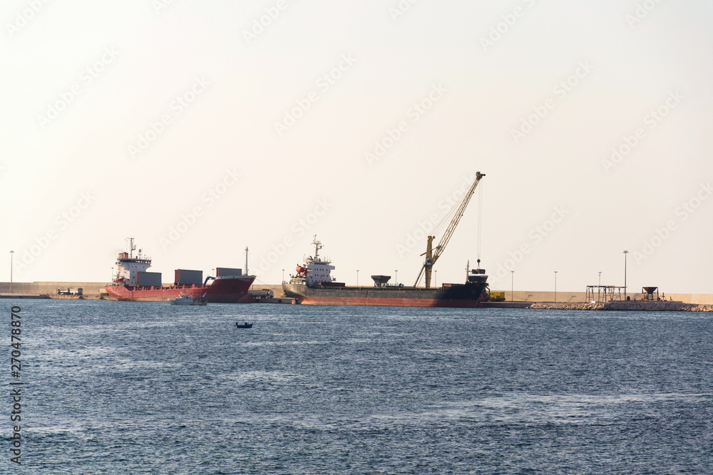 Yellow crane unloading sand from large freighter cargo ship in harbor, freight digitalization, transportation efficiency, sand shortage concept, sunny day copy space
