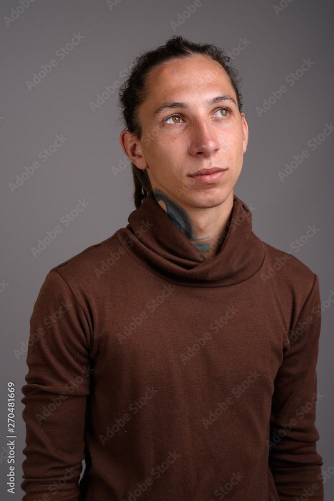 Young man with dreadlocks wearing brown shirt against gray backg Young man with dreadlocks wearing brown shirt against gray backg