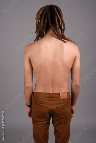 Young shirtless man with dreadlocks against gray background 