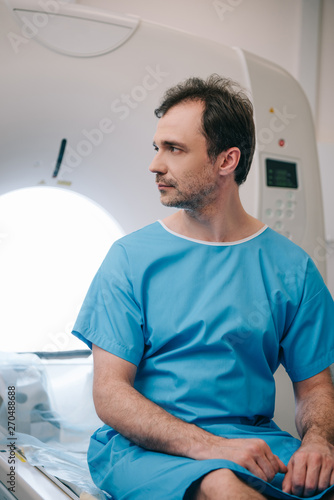 handsome man sitting on ct scanner bed in hospital and looking away