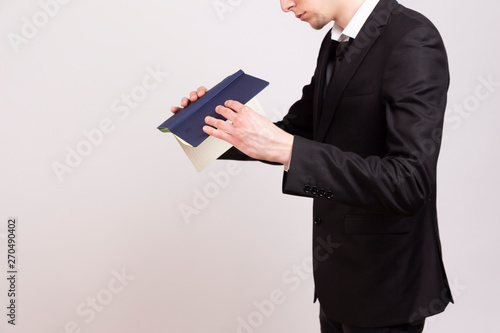  A young man in a black jacket, white shirt and black tie is looking for something in a notebook