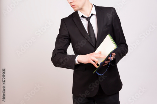  A young man in a black jacket, white shirt and black tie points his finger at the pages of a notebook