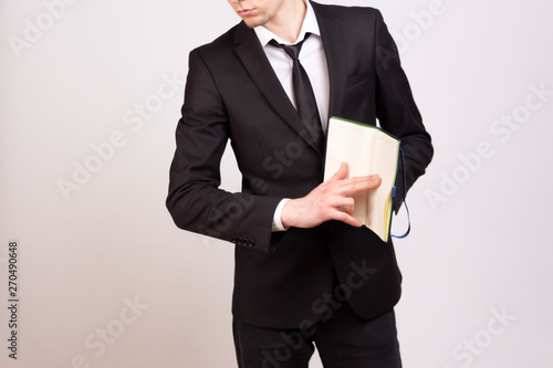  A young man in a black jacket, white shirt and black tie points his finger at the pages of a notebook