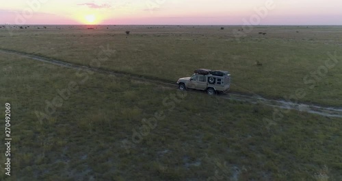 Tracking shot of safari vehicle driving through the grasslands of Botswana into the setting sun photo