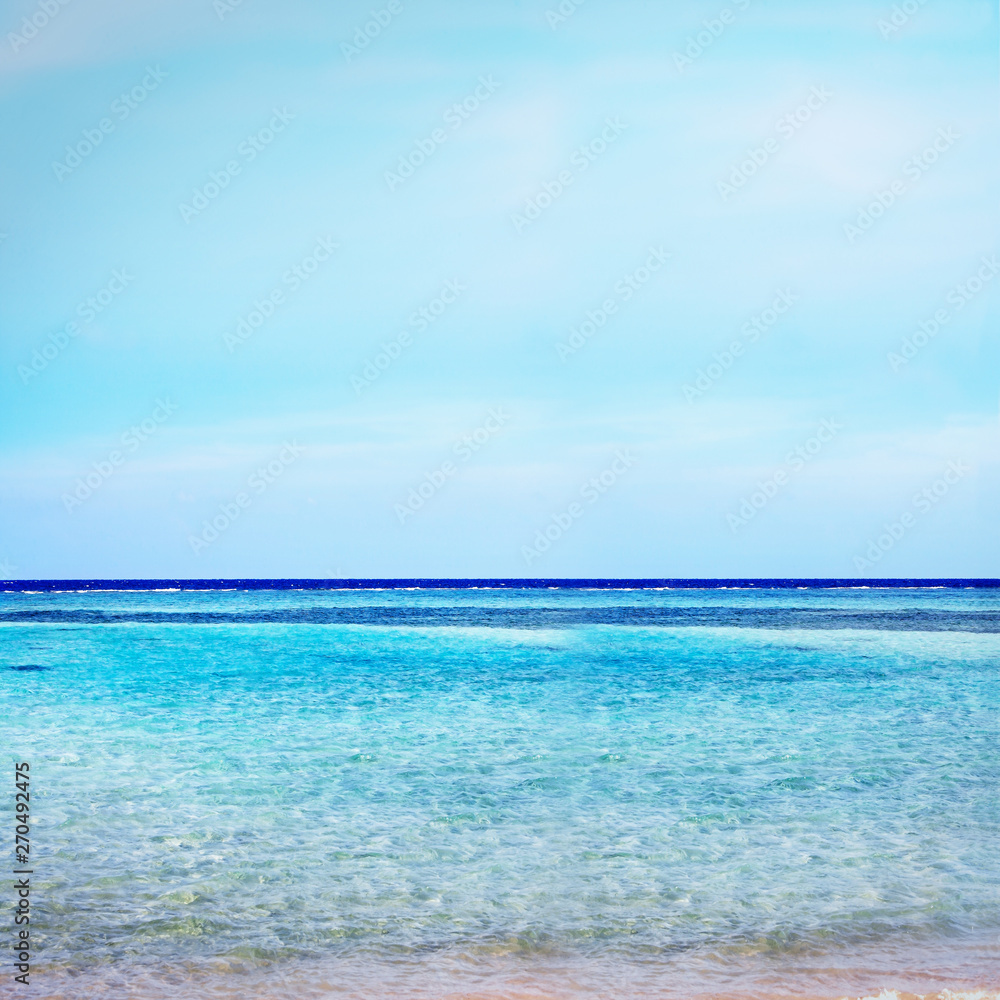 Beach on crystal with azure ocean and blue sky horizon background.