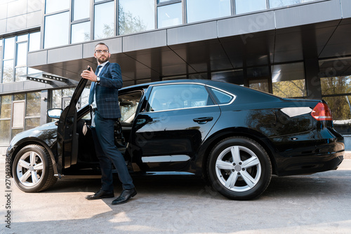 low angle view of handsome businessman in suit standing near black car © LIGHTFIELD STUDIOS