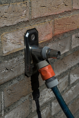 Outside metal water tap sticking out of normal house wall bricks. House water tap with a waterhose attached.