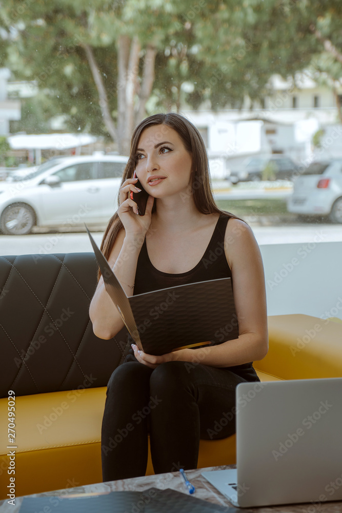 Fototapeta premium young business woman talking on mobile phone at office with document file folder.