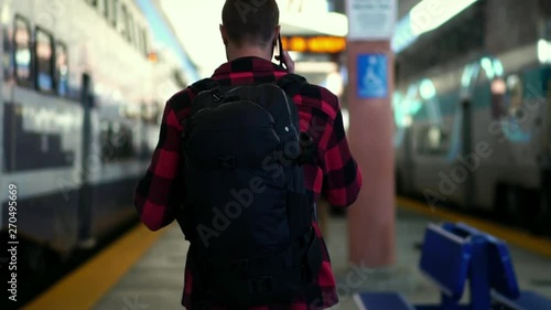 Slow motion: Beautiful young male walking on train platform at Los Angeles train station. Concept of travel active lifestyle, millennial urban life, summer vacation. photo